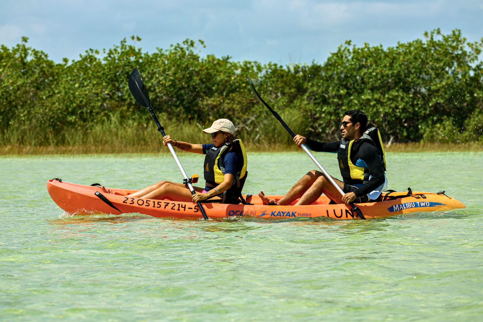 Couple paddling an orange kayak across the turquoise lagoon in Sian Ka an